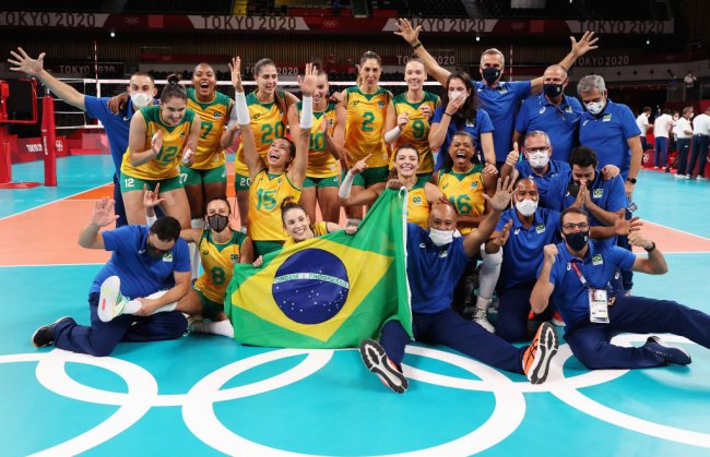 Jogadores e equipe técnica do Brasil posa para foto após vaga garantida na semifinal. Eles estão felizes, com os braços para a cima e segurando a bandeira do Brasil