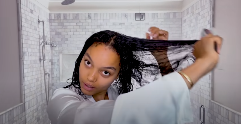Whitney Peak de roupão, em um banheiro, penteando o seu cabelo.