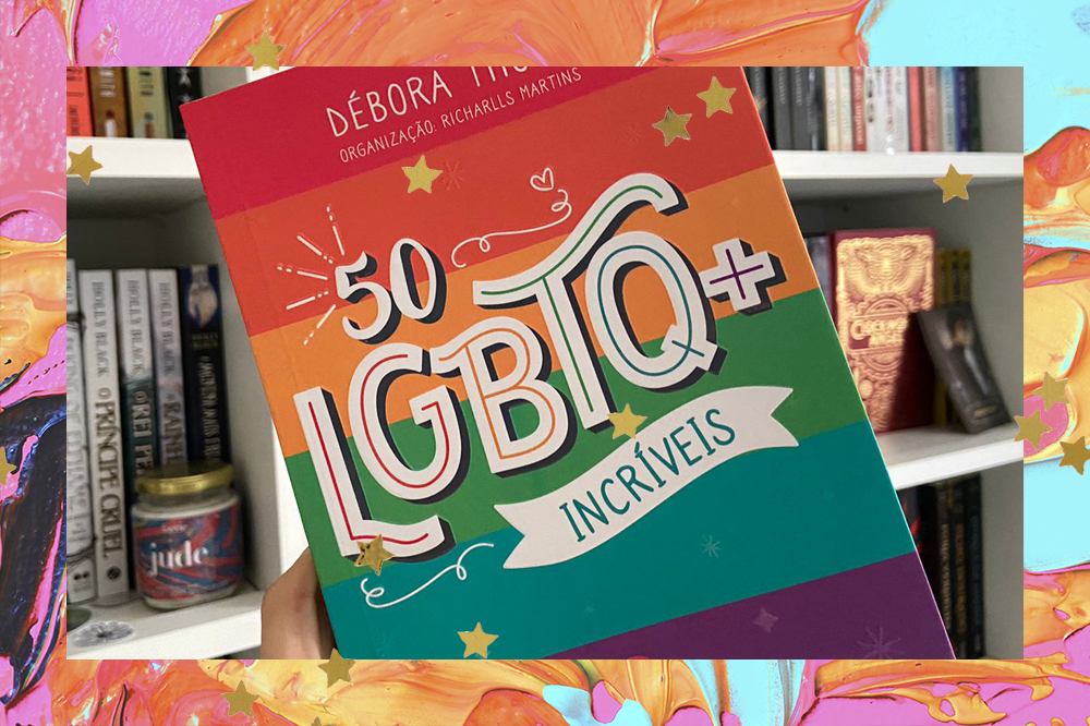 Foto do livro 50 LGBTQ+ Incríveis, livro de Débora Thomé com organização de Richarlls Martins; o exemplar está sendo segurando na frente de uma estante branca com outros livros e artigos de decoração literária como velas e cards; a capa é listrada com as cores da bandeira LGBTQ+ e o título está em destaque no centro da capa; a margem é uma textura de tintas nas cores amarela, azul, rosa, laranja e estrelas amarelas decoram a imagem