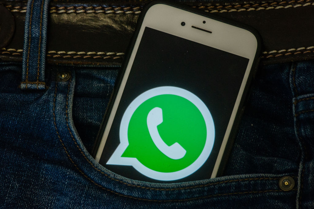 Foto de um iphone no bolso de uma calça jeans. Na tela, aparece o logo do WhatsApp
