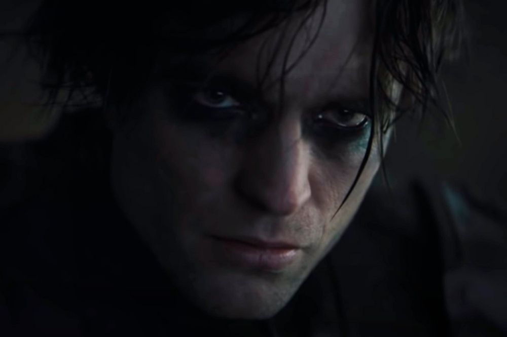 Foto do ator Robert Pattinson como Batman. Nela, ele aparece com uma expressão séria e rosto manchado de preto.