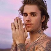 Foto de Justin Bieber para divulgação; ele está sem camisa com as mãos juntas na frente do rosto e olha para câmera com expressão séria