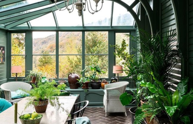 Saiba como se hospedar na casa do Otis e no trailer de Maeve, de Sex Education Foto de uma sala de jantar verde, cheia de janelas, bem arejada, com muitas plantinhas