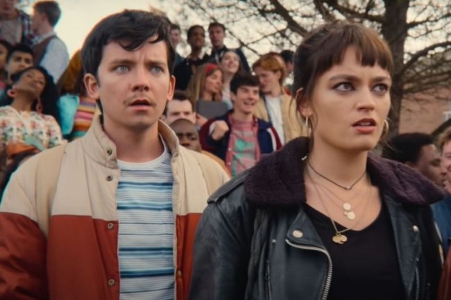 Foto da série Sex Education. Nela, aparece dois adolescentes com cara de indignação e choque: um menino de camisa listrada e jaqueta; uma menina com franja e jaqueta de couro preta.