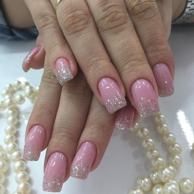 Foto de uma mão segurando um esmalte e exibindo as unhas com glitter nas pontas.