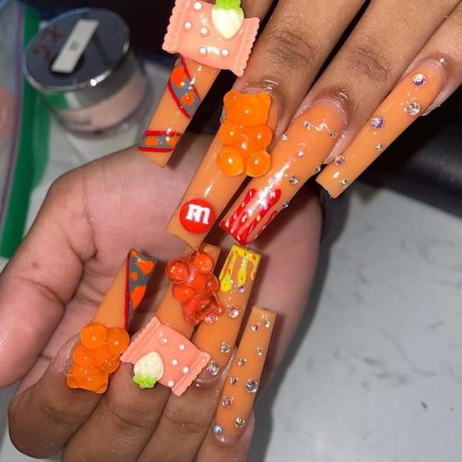 unhas-nail-art-doces Foto de unhas grandes com esmalte laranja e detalhes de decorações 3D de doces coloridos.
