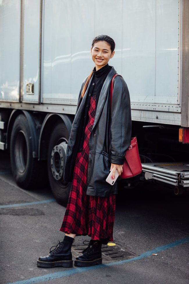 Jung Ho-yeon posando sorridente com vestido xadrez e blusa escura.