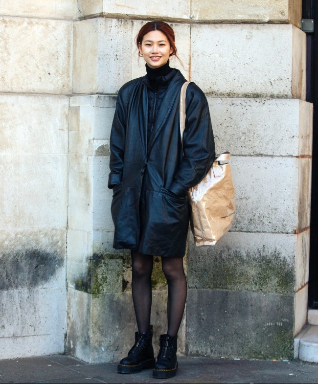 Jung Ho-yeon posando sorridente com bolsa na lateral do corpo meia calça preta e coturno.