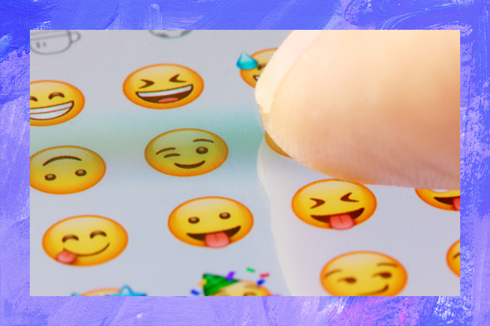 Foto do dedo de uma mulher selecionando um emoji na tela do celular