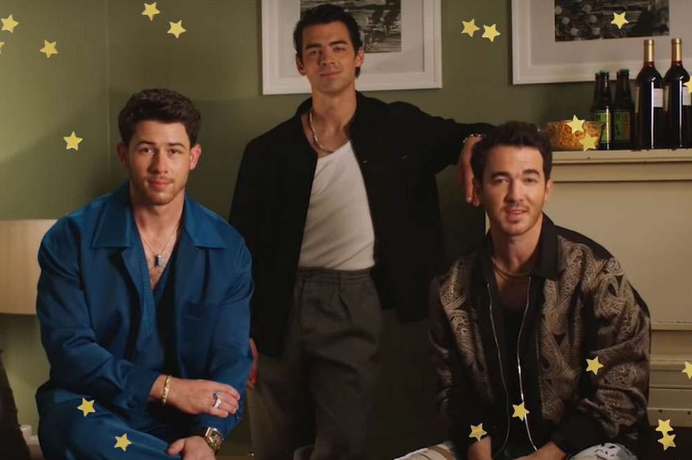 Foto dos irmãos Jonas. Nela, eles estão posando lado a lado: Nick na esquerda com roupa social azul, Joe no centro e Kevin sentado à direita.