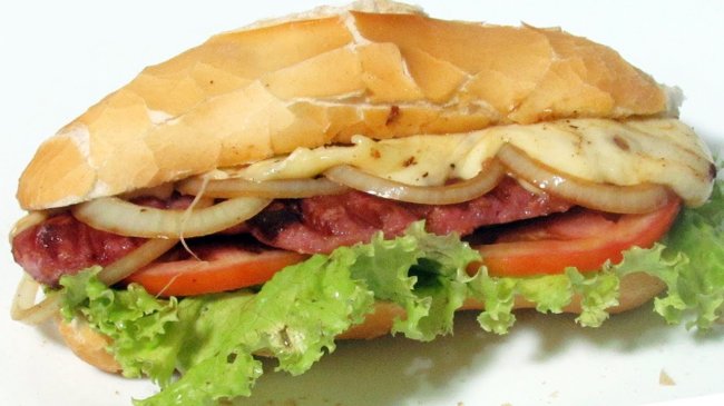 Foto de um pão recheado com linguiça, cebola, alface, queijo e tomate