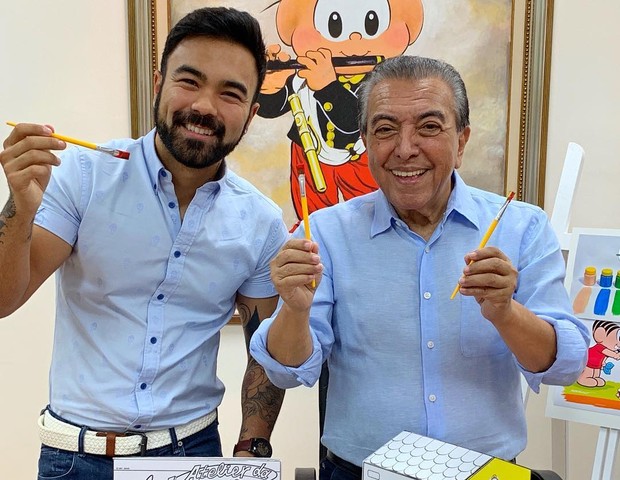 Maurício de Sousa com seu filho, Mauro. Eles seguram pinceis cheios de tintas coloridas