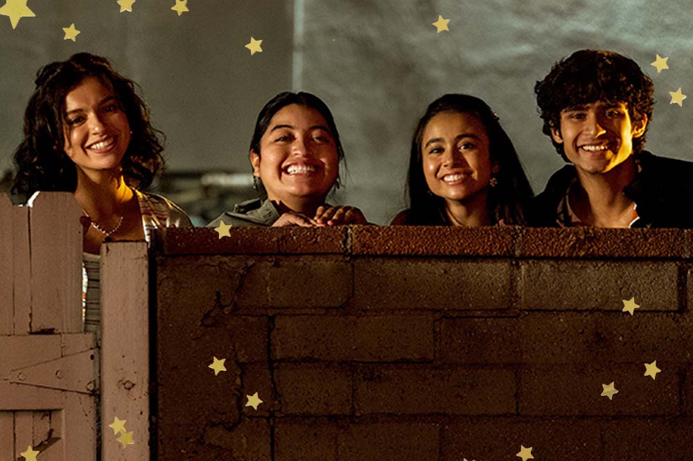 Foto de quatro pessoas sorrindo atrás de uma parede de tijolos.