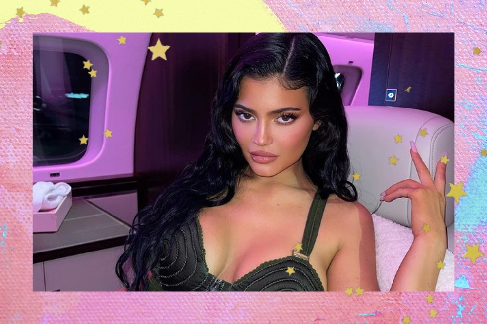 Montagem com o fundo rosa e amarelo com detalhe de estrelinhas douradas com a foto da Kylie Jenner. Na foto ela usa um top preto, cabelo solto e maquiagem. Ela olha para a câmera e não sorri.