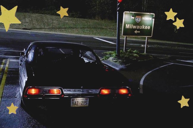 Imagem de um carro Impala aguardando na estrada, ao lado de uma placa de trânsito. Está de noite.