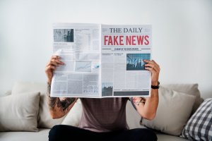 Um jovem com os braços tatuados lendo jornal. Na capa, uma notícia sobre fake news. Não dá para ver o rosto, que está coberto pela publicação