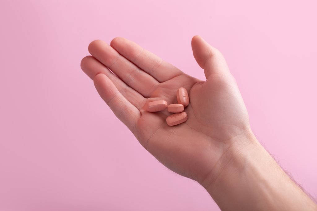 Foto de uma mão segurando pílulas rosas de tratamento contra o HVI; o fundo da imagem também é rosa claro