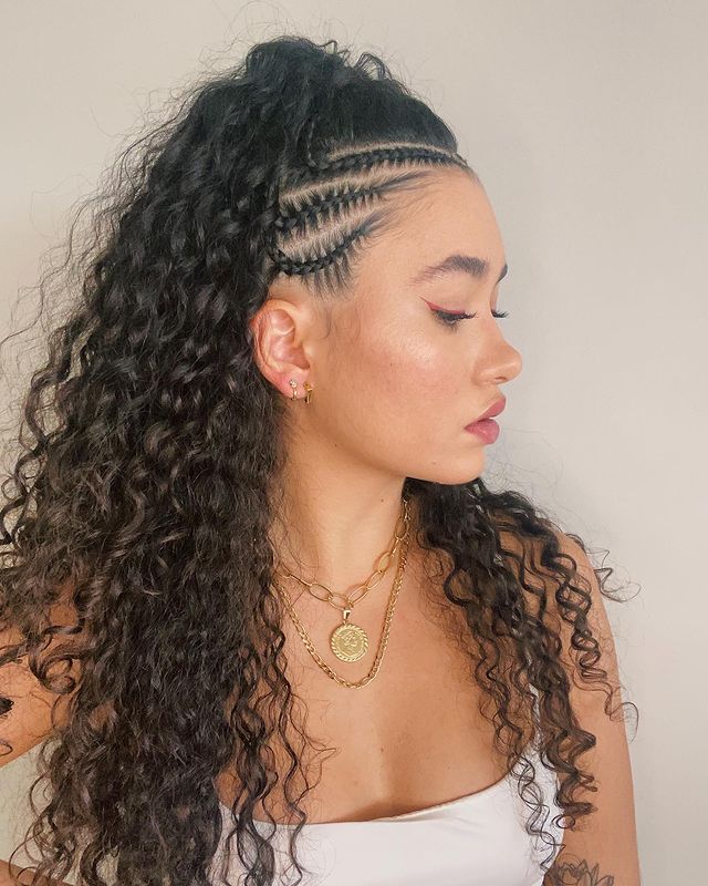 Foto de uma mulher de perfil. Ela usa um top cropped branco, colares dourados, cabelo cacheado solto com trança lateral na raiz do cabelo. Ela está de perfil, não olha para a câmera e não sorri.