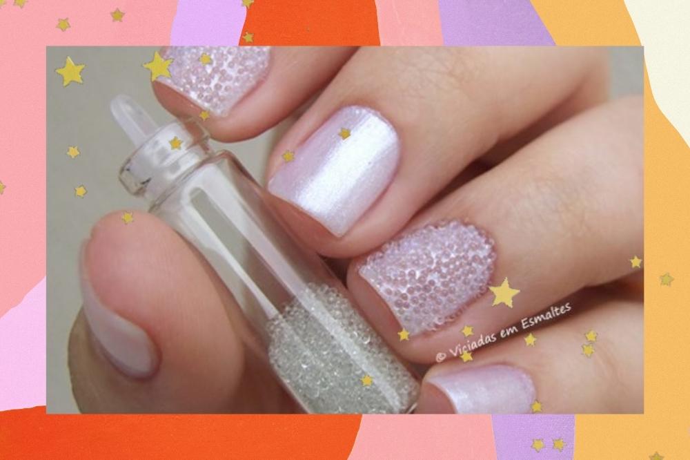 Imagem com o fundo colorido e detalhes de estrelinhas douradas com a foto de uma mão segurando um potinho com bolinhas brancas para nail art com as unhas brancas com detalhe de bolinhas que imitar o caviar.
