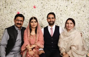 Foto do casamento de Malala. A família está reunida em frente a uma parede de rosas brancas. Todos sorriem.