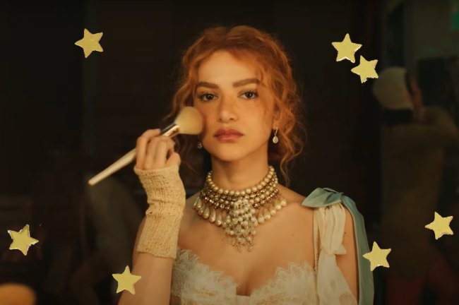 Manu Gavassi lança GRACINHA, o grito de liberdade da garota de headband Cena do clipe de Bossa Nossa, da Manu Gavassi. Ela olha para a câmera enquanto passa um pincel de pó pelo rosto