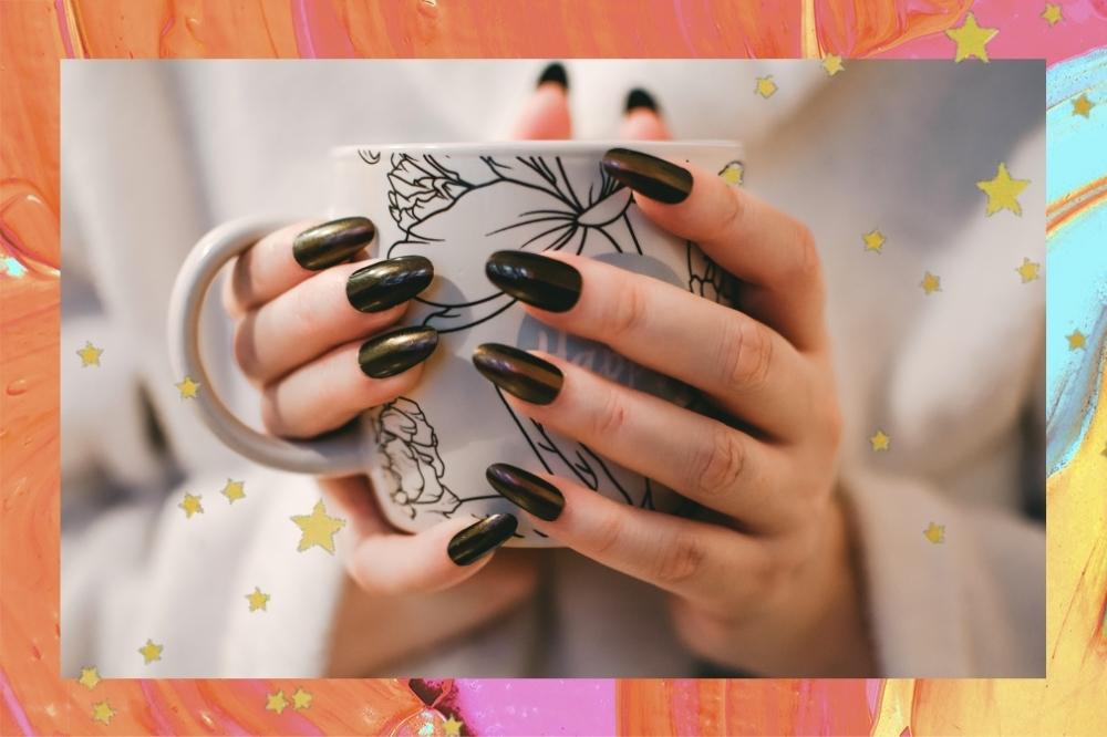 Montagem com o fundo laranja e detalhe de estrelinhas douradas com a foto de uma mão com a unha grande e esmalte preto segurando uma xícara.