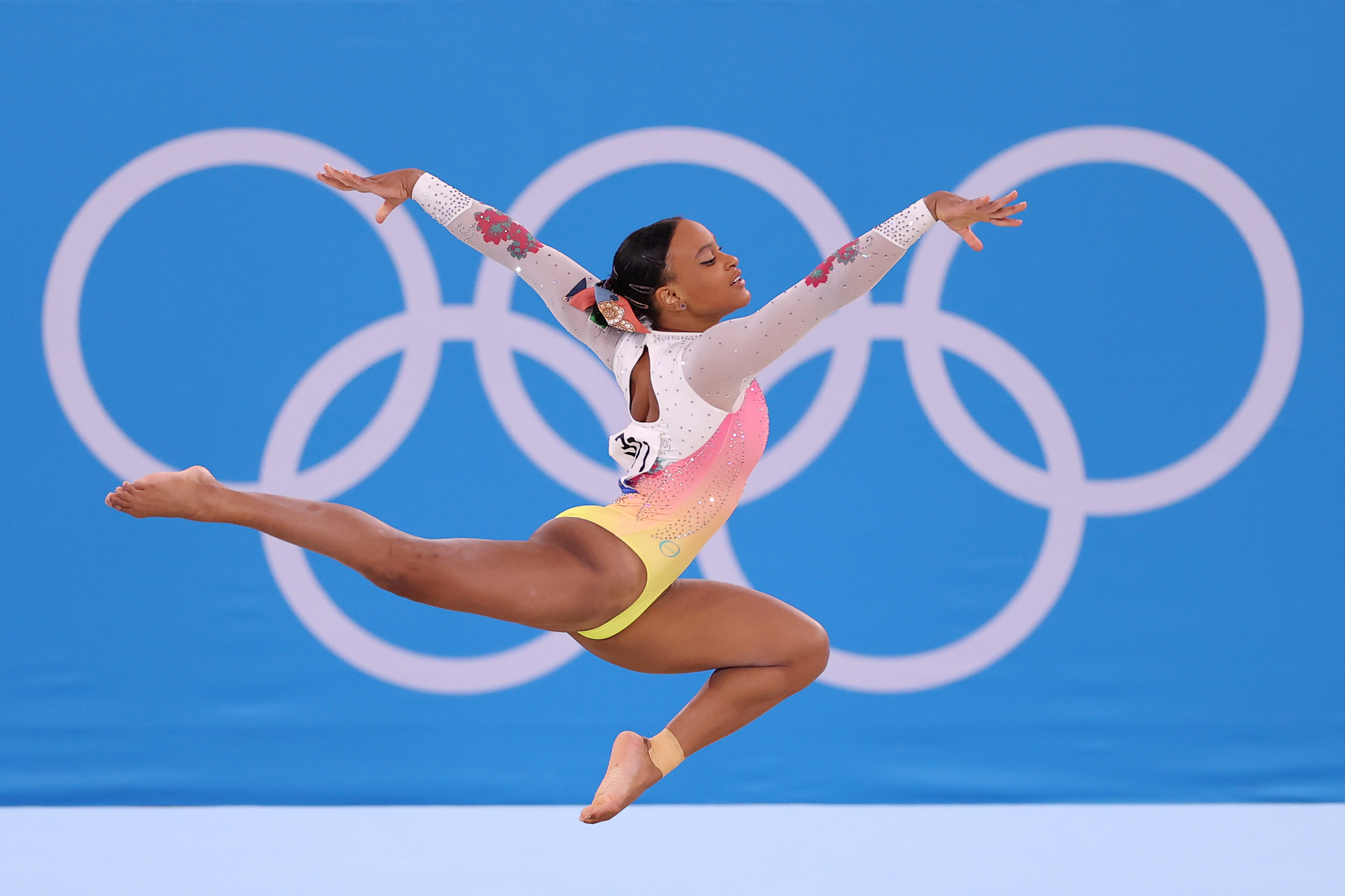 A ginasta Rebeca Andrade competindo nas Olimpíadas de Tóquio usando collant branco, rosa e amarelo