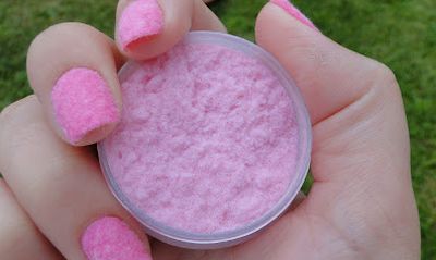 Foto de uma mão segurando um potinho com camurça rosa para nail art e unhas rosas decoradas com camurça.