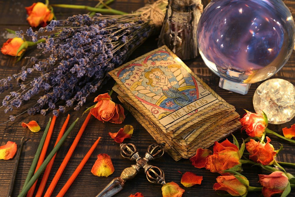 Carta dos Enamorados, do Tarot, em cima de uma mesa cheia de cristais, flores e velas