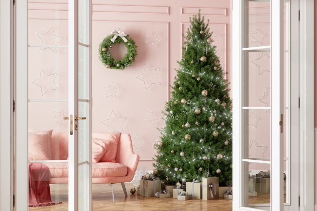Foto de uma sala rosa, com um sofá rosa, e uma árvore de natal no cantor. Ao lado, na parede, uma guirlanda pendurada