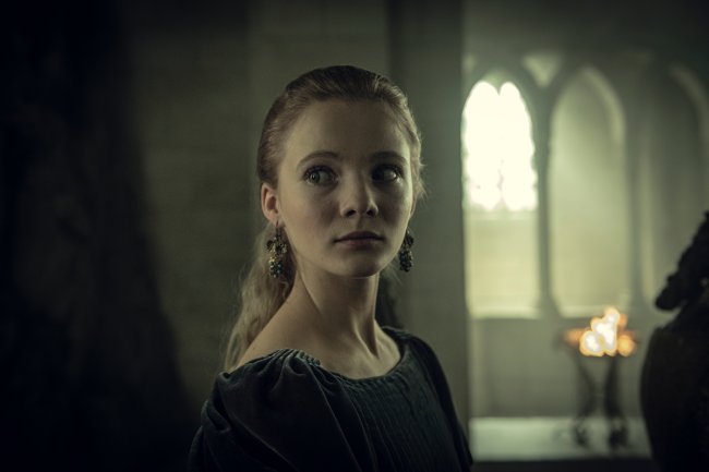 WW_101_29.11.2018_144.NEF Cirila (Freya Allan) em The Witcher, da Netflix; a personagem está olhando para o lado com expressão assustada; ela usa um vestido verde escuro com brincos dourados com verde e o cabelo preso; ela está em um quarto com grandes janelas ao fundo