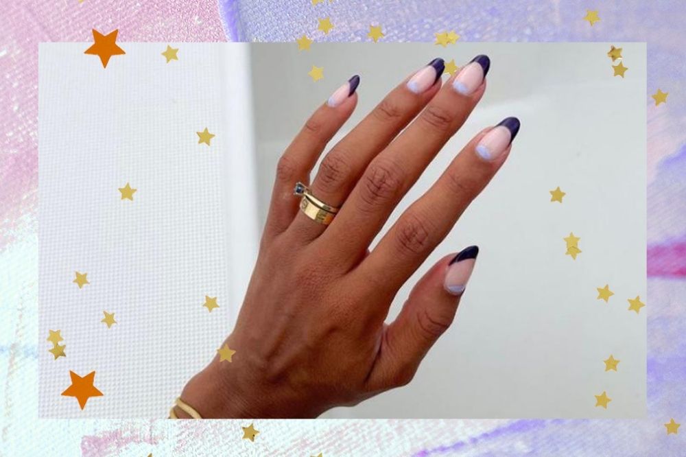 Mão com nail art em formato meia lua com francesinha em azul escuro e claro pastel, bem como dois anéis dourados no dedo anelar esquerdo. O fundo da montagem é em tons pastel e possui estrelas douradas.