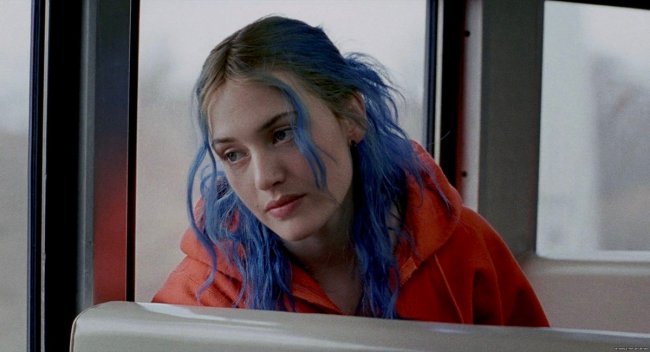 Foto de Kate Winslet com o cabelo azul no filme Brilho Eterno de uma Mente Sem Lembranças. Ela está com cara de tédio e encosta a cabeça em uma janela