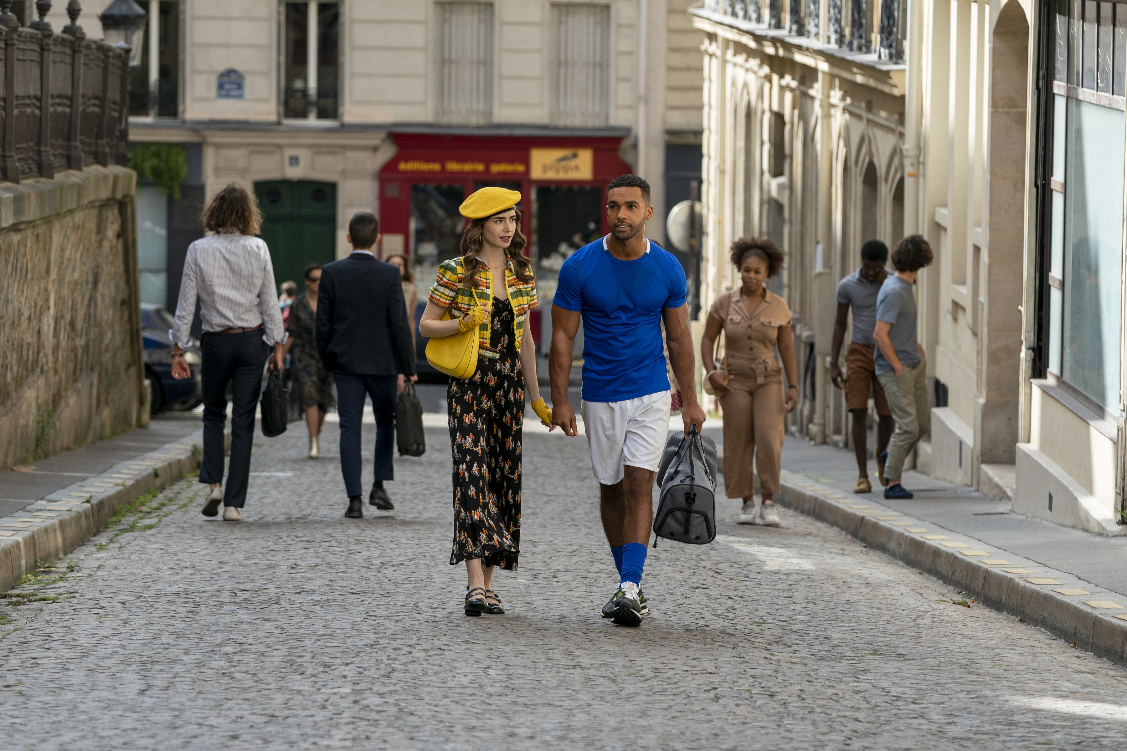 Lily Collins como Emily e Lucien Laviscount como Alfie de mãos dadas na série Emily em Paris