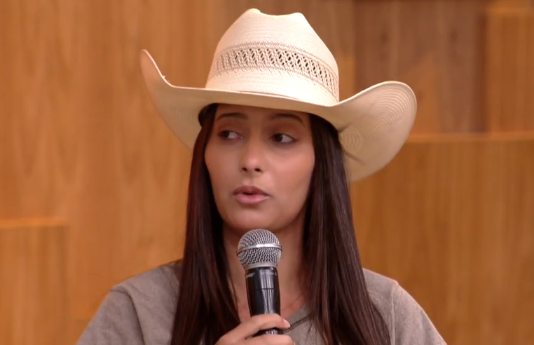 Foto de Franciane Andrade falando durante programa com Fátima Bernardes. Ela tem o cabelo castanho liso e comprido, usa um chapéu de boiadeiro bege e uma camiseta marrom claro