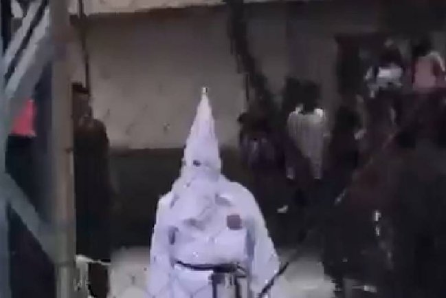 Imagem de um homem vestido com as características roupas da Ku Klux Klan. Elas são brancas e tem um chapéu pontudo que cobre todo o rosto