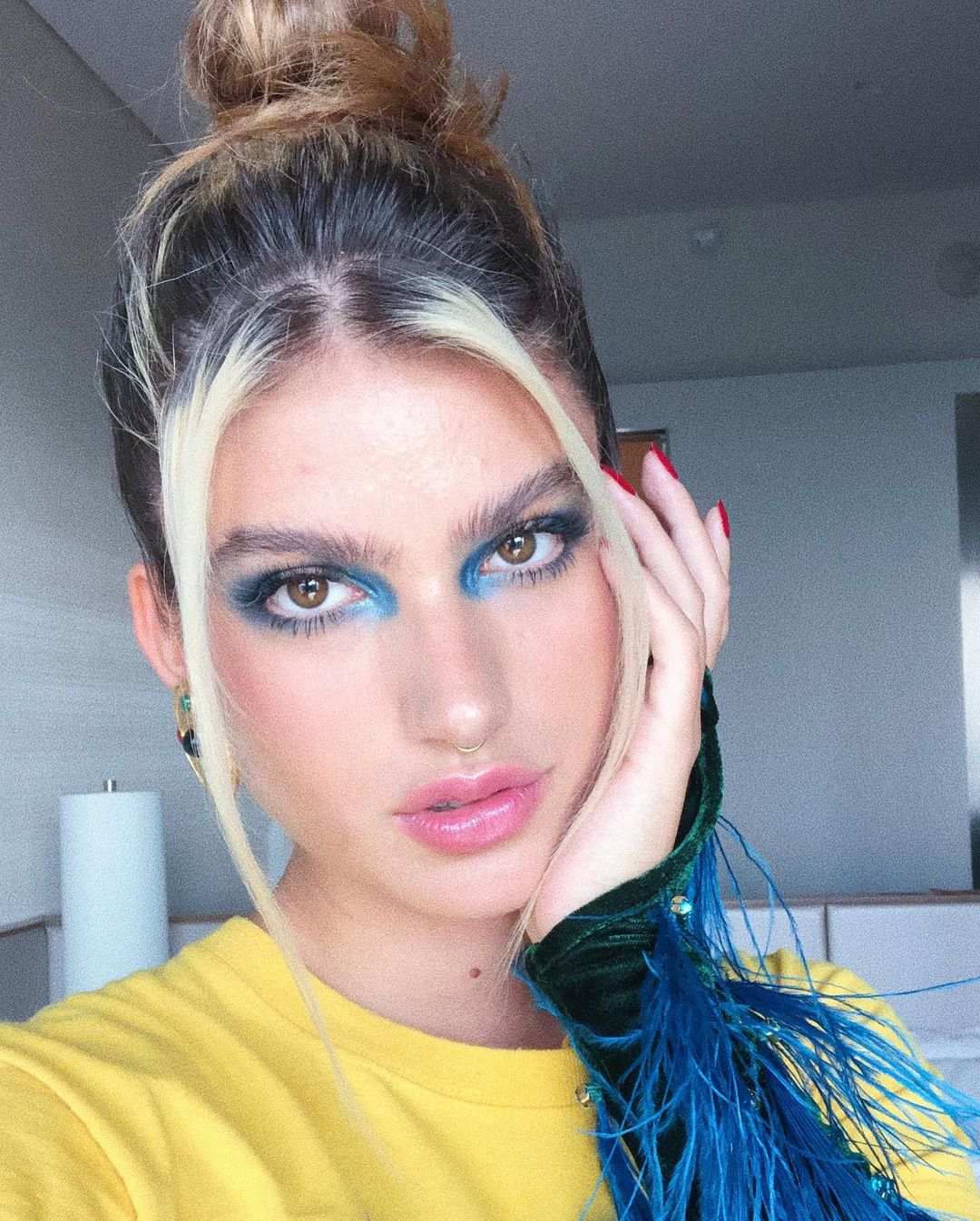 maquiagem-giovanna-grigio Giovanna Grigio usando sombra azul, com expressão facial séria, cabelo preso em um coque e uma das mãos apoiadas no queixo