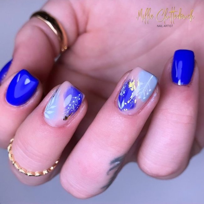 Foto de uma mão com anéis dourados no dedo polegar e médio com as unhas decoradas em tons de azul.