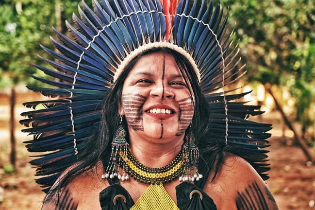 Foto da ativista Sônia Guajajara. Ela é uma mulher indígena, aparece com cocar e pinturas faciais de sua tribo