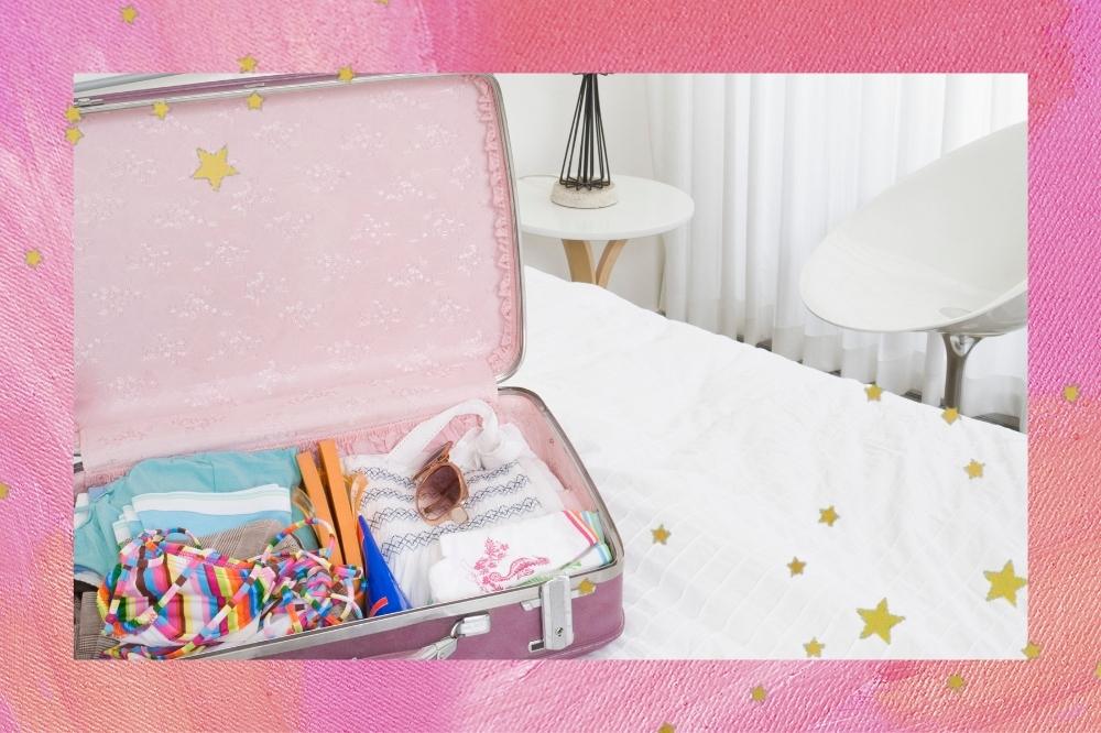 Montagem com o fundo rosa, detalhe de estrelinhas douradas com a foto de uma mala de viagem rosa em uma bolsa com roupas e produtos dentro.