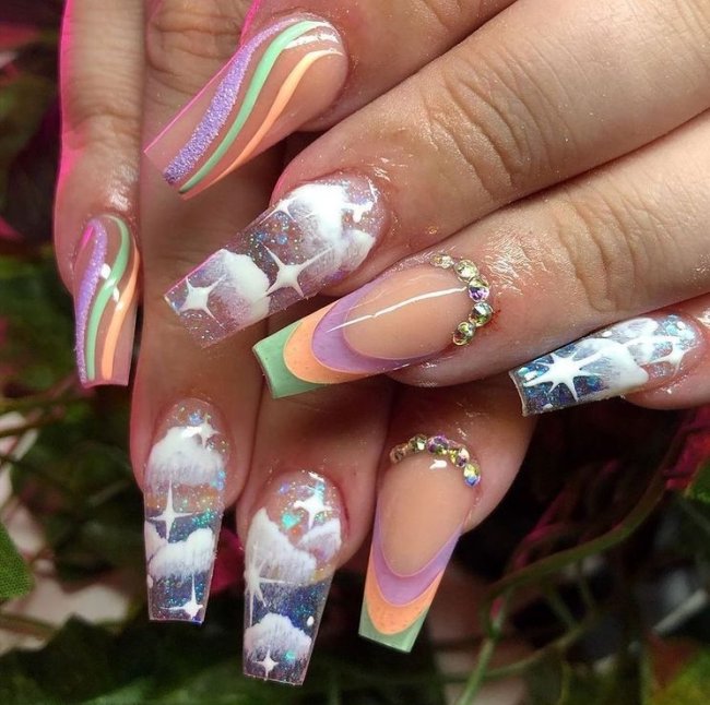 Foto de duas mãos com as unhas coloridas com decoração de nuvens brancas.