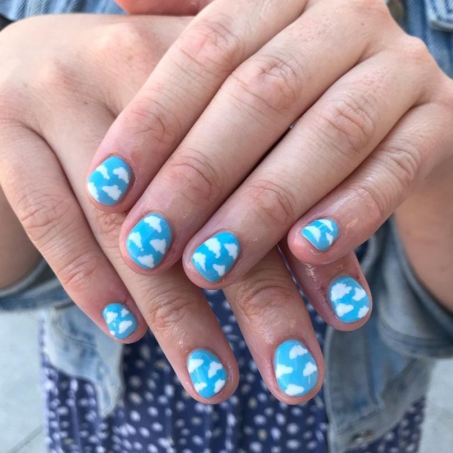 Fotos de mãos com as unhas decoradas com esmalte azul e decoração de nuvens brancas.