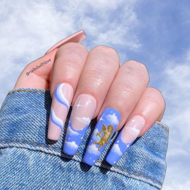 Foto de uma mão com o fundo de nuvens. As unhas dessa mão estão decoradas com esmalte azul e detalhes de nuvens e anjinhos.