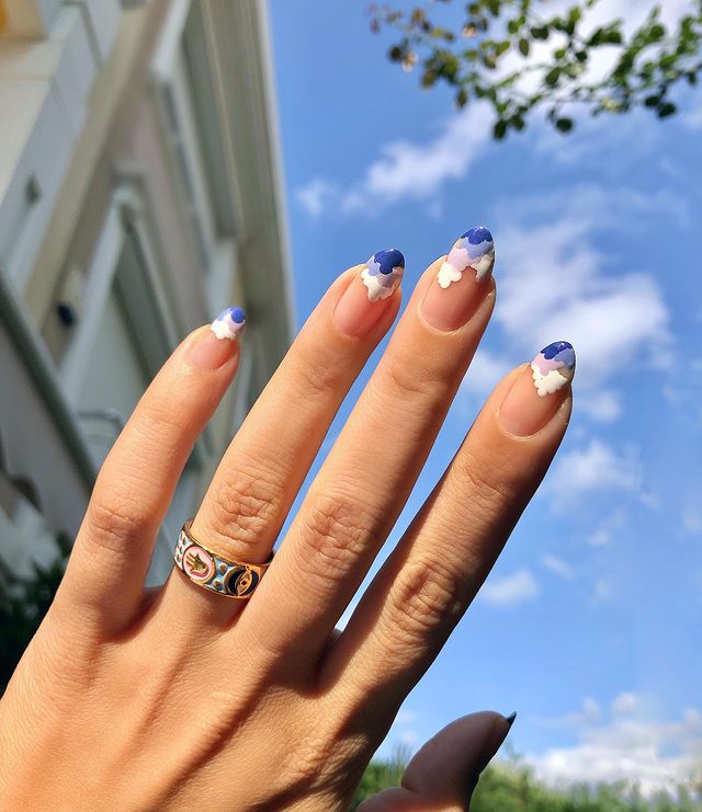 Foto de uma mão com as unhas decoradas com nuvens coloridas na ponta da unha.