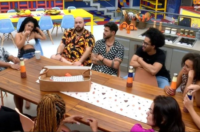 Print da imagem da câmera do Big Brother Brasil. As pessoas estão reunidas, sentadas na mesa do cozinha.