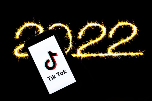 Foto de um celular mostrando a tela de início do TikTok. Ao fundo, 2022 escrito em dourado