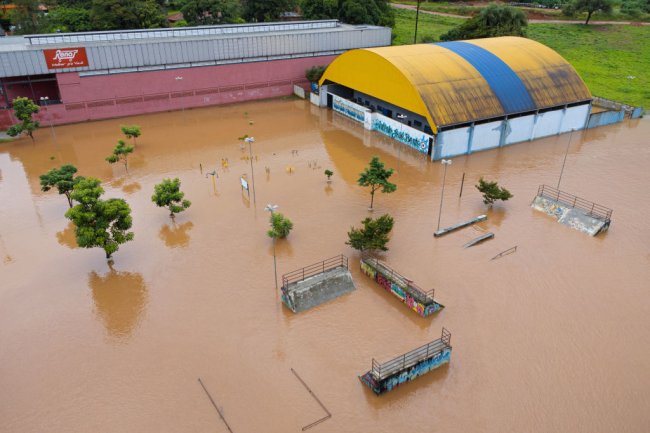 Foto aérea de uma cidade mineira completamente alagada. Dá para ver o ginásio de uma escola com água até o teto praticamente