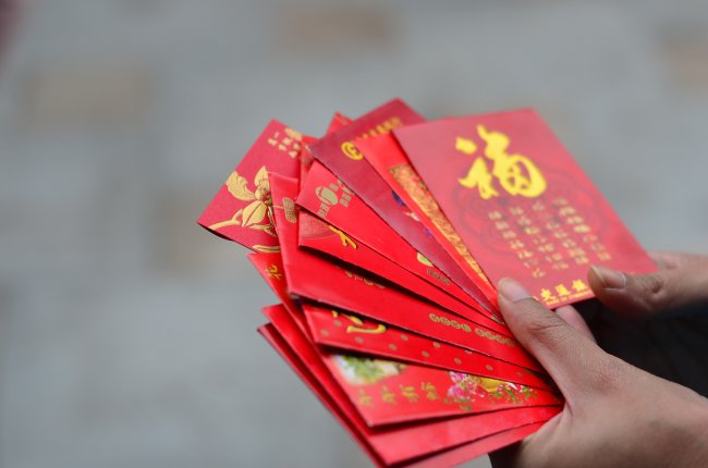 Uma mão segurando várias cartas vermelhas com escritos em chinês na cor dourado