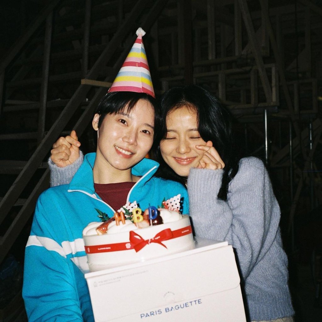 Kim Mi Soo e Jisoo junas sorrindo abraçadas enquanto uma delas segura um bolo e usa chapéu de aniversário