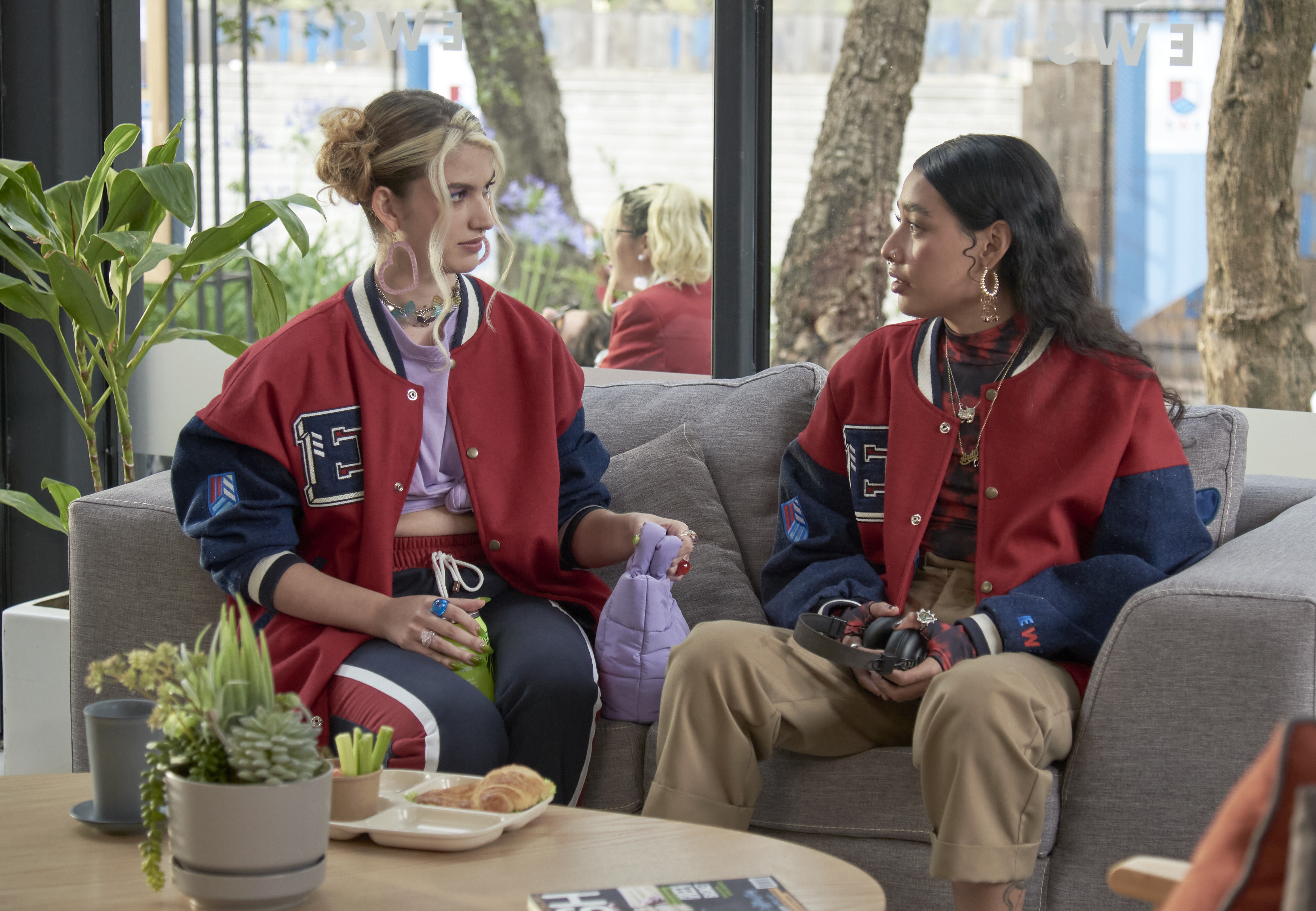 As personagens Emilia e Andi sentadas em sofá em cena da série Rebelde, da Netflix